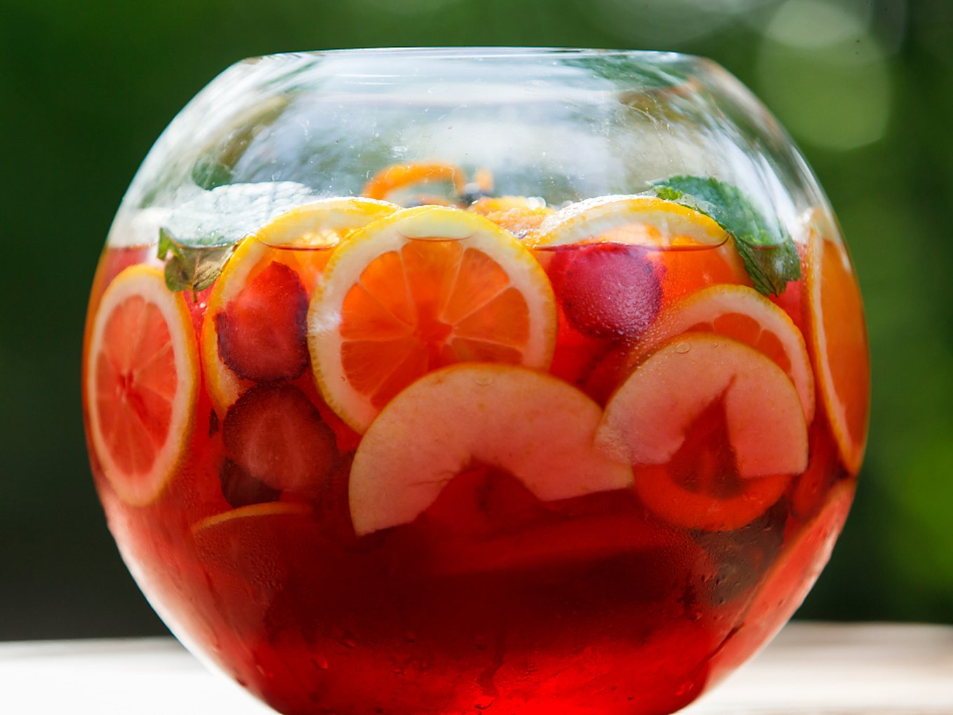 Große Bowleschüssel mit Zitronen-, Orangen- und Apfelscheiben im Garten