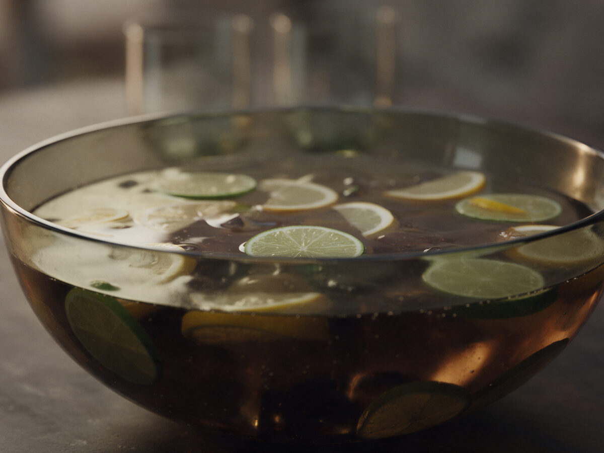 Dunkle Cola-Bowle mit Limetten- und Zitronenscheiben in einer großen Rauchglasschüssel