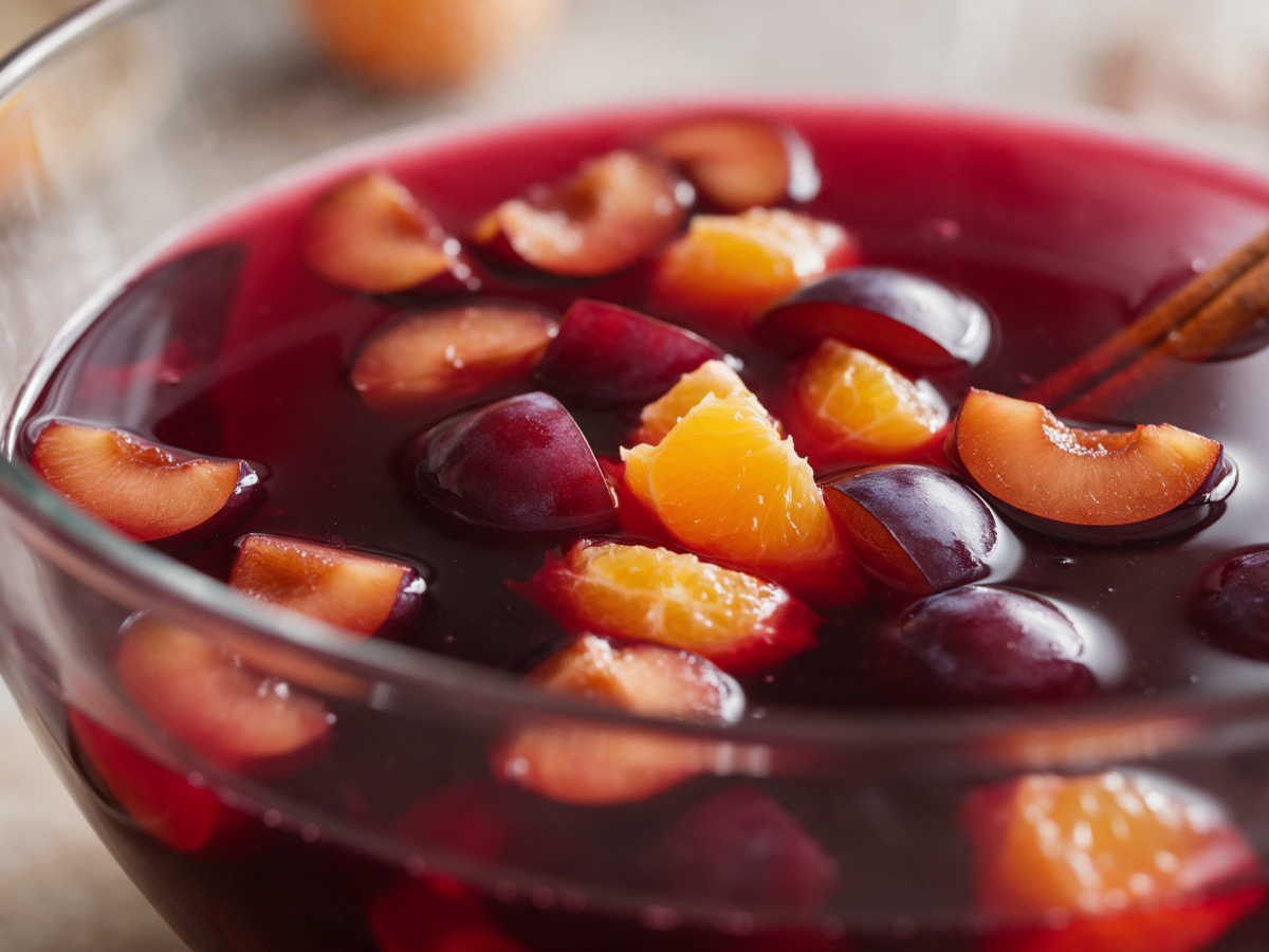 Pflaumen-Rotwein-Bowle mit Pflaumenstücken, geschälter Orange und Zimt in einer großen Glasschüssel