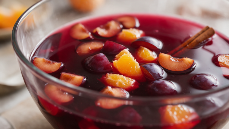 Pflaumen-Rotwein-Bowle mit Pflaumenstücken, geschälter Orange und Zimt in einer großen Glasschüssel